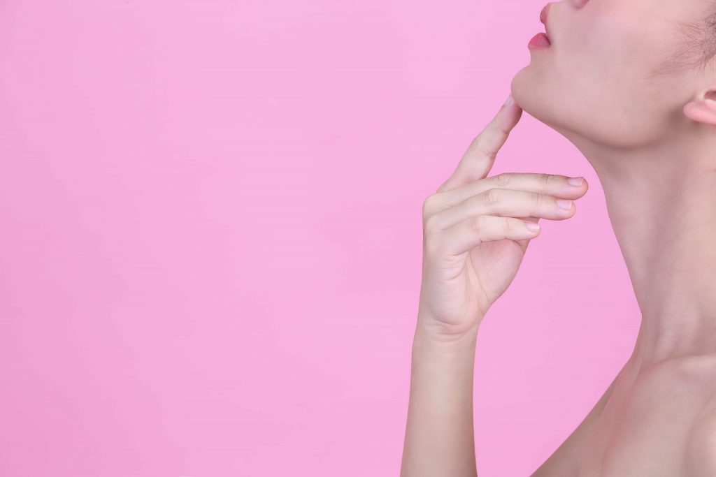 beautiful young woman is touching her chin with her index finger pink wall 1 1024x683 1