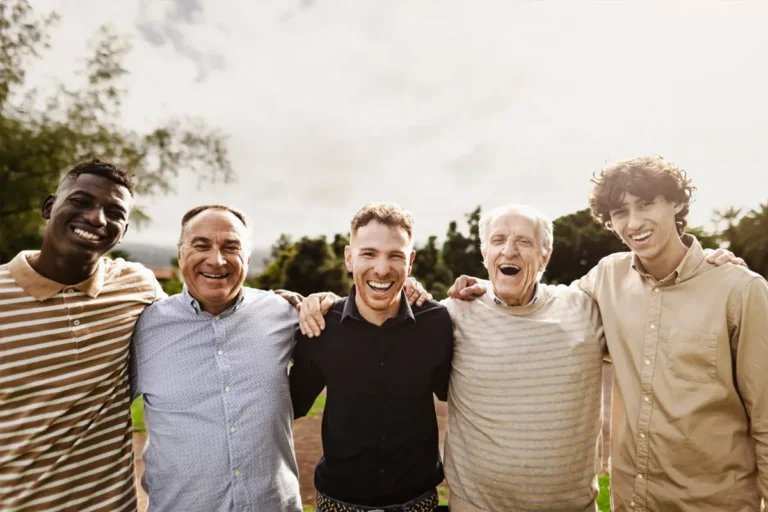 five men of different ages smiling and standing arm-in-arm outdoors